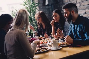 Amigos comiendo en un restaurante con paneles acústicos artísticos.